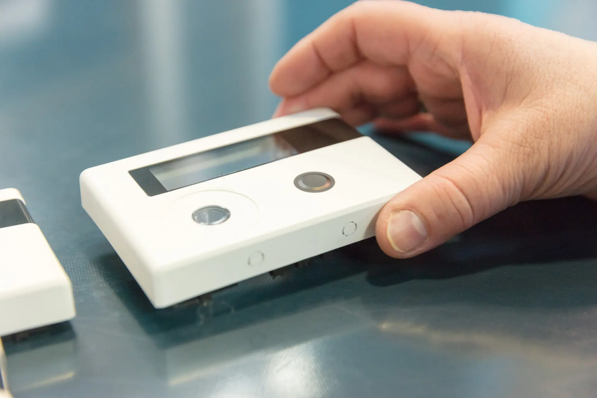 Hand holding a white device housing with display and buttons.